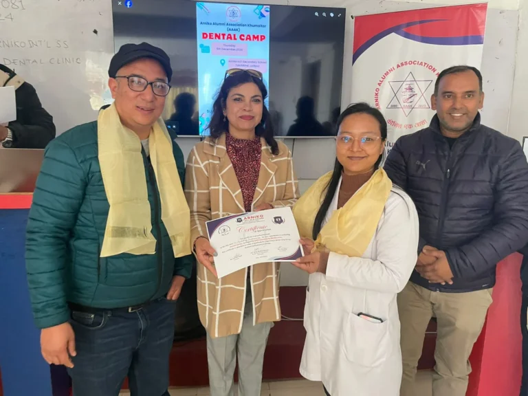 दन्त शिविरको पोस्टर देखिएको स्क्रिन र AAAK ब्यानरअगाडि प्रमाणपत्र समातेका चार जना