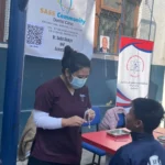 बसेका विद्यार्थीछेउ उपकरण तयार गर्दै दन्त स्वास्थ्यकर्मी, पछाडि क्लिनिक र AAAK का ब्यानर