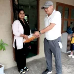 सानो विद्यार्थीले हेरिरहँदा कक्षाकोठाको ढोकामा कापीको चाङ लिँदै शिक्षिका