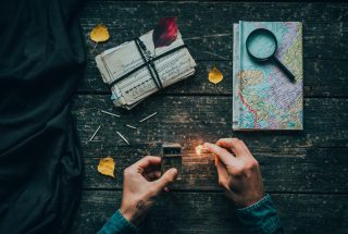 A creative flat lay featuring a map, letters, and a match being ignited on a vintage wooden table.